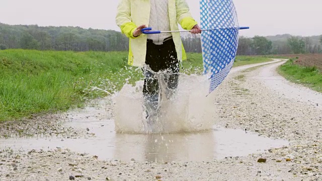 小女孩拿着雨伞走在泥泞的水坑里视频素材