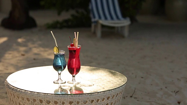 热带海滩的桌上有两杯鸡尾酒。蓝色和粉色饮料视频素材