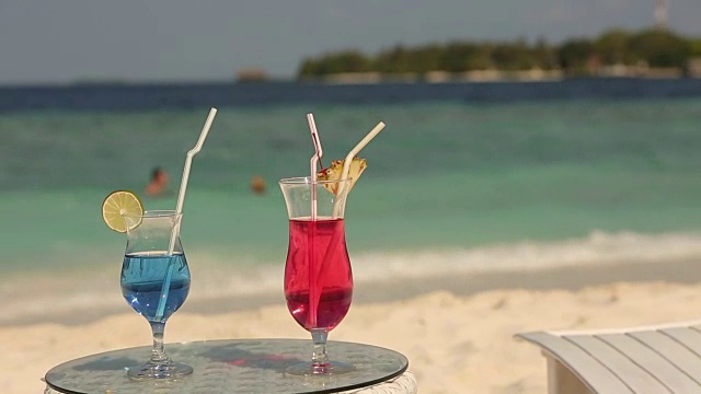 热带海滩的桌上有两杯鸡尾酒。蓝色和粉色饮料视频素材