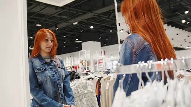 年轻的模特女孩正在一家女装店里挑选一件牛仔夹克视频下载