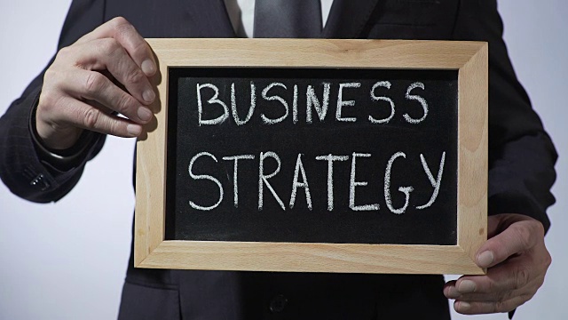 商业战略写在黑板上，男人穿着黑色西装举着牌子，事业有成视频下载