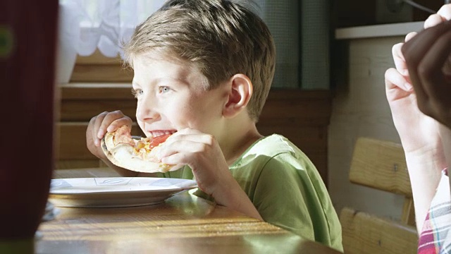 小男孩在桌子上吃着一片披萨视频素材