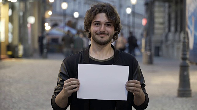 快乐微笑的少年男子在城市的街道上举着一个空白的拷贝空间横幅视频素材