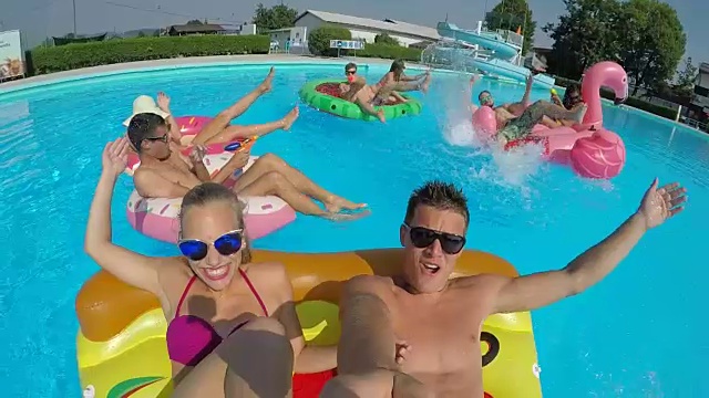 在泳池派对上，欢快的朋友们在有趣的浮舟上打水仗视频素材