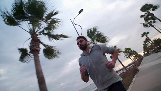 一个戴着耳机的年轻人在海边跑步视频素材