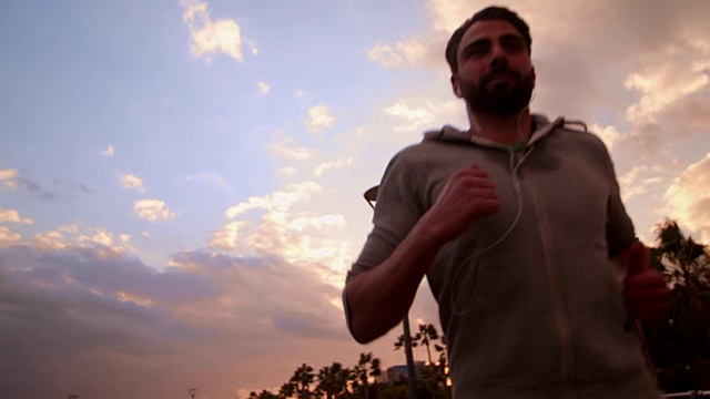年轻的男运动员在日落边跑步边听音乐视频素材
