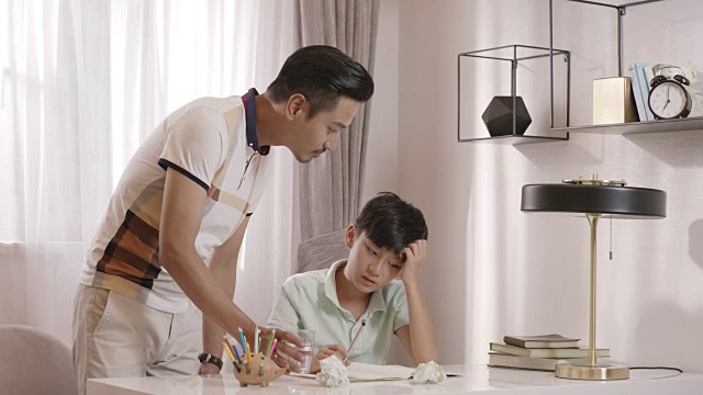 一位亚洲父亲走进阅览室，和儿子聊天，儿子正在做作业视频下载