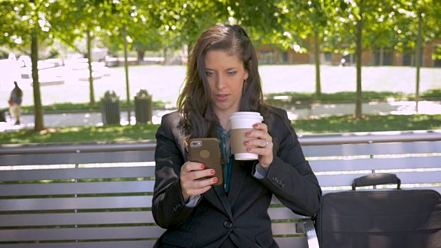 在公园长椅上看手机应用技术的美女视频素材