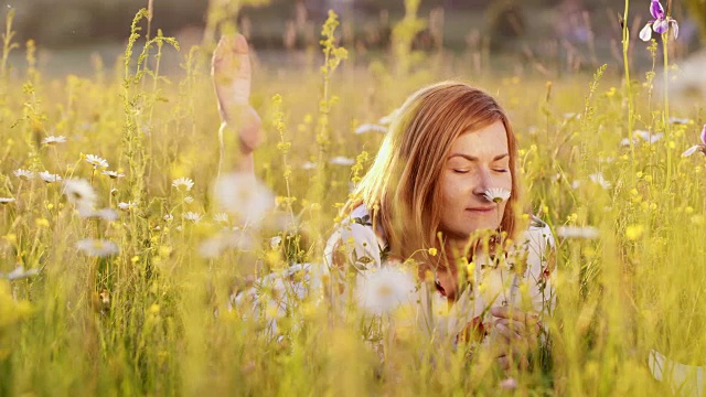 一个女人在春天的草地上嗅着一朵雏菊视频下载