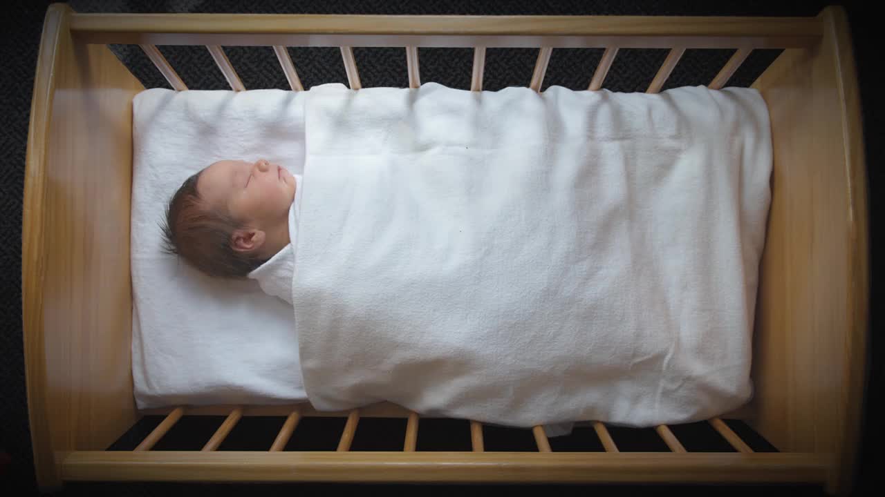 新西兰奥克兰，宝宝睡在白色毯子下的婴儿床里视频下载