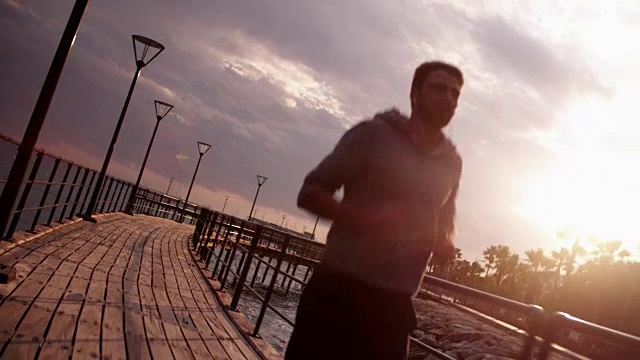 年轻的健康男子在日落边跑步边听音乐视频素材