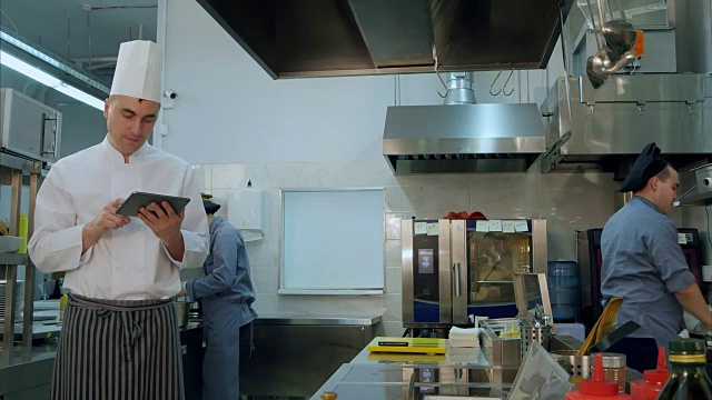 厨师在专业厨房的平板电脑上查看食谱视频素材