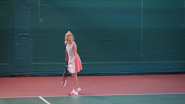 小女孩穿着运动服在室内网球场训练。年轻的女运动员正在打职业网球，在用球拍击球前弹起黄色的球视频下载