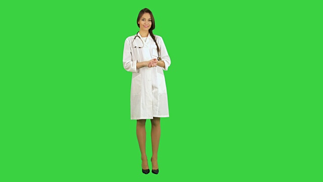 年轻漂亮的女医生穿着实验服，带着听诊器看着绿屏上的摄像头视频下载