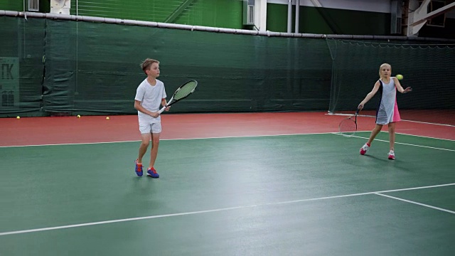两个快乐的孩子在球场上用球拍发球和接球训练技巧。漂亮的男孩和女孩在娱乐区玩运动游戏。未来的职业选手正在上网球课视频下载