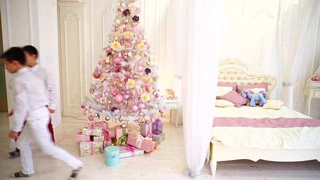 两个男孩白天在明亮的卧室里，在圣诞树下为父母准备了儿子的新年礼物视频素材