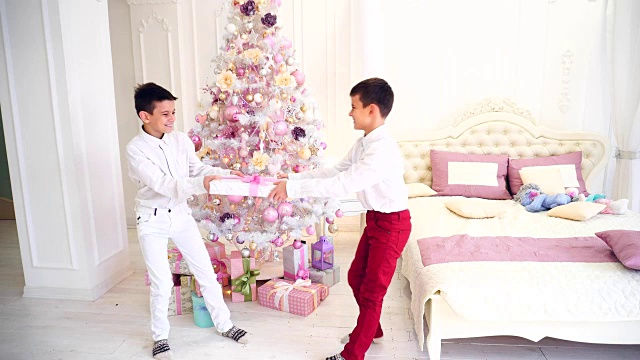 两个双胞胎兄弟的幼稚恶作剧和无辜的战斗圣诞礼物在卧室的圣诞树视频素材