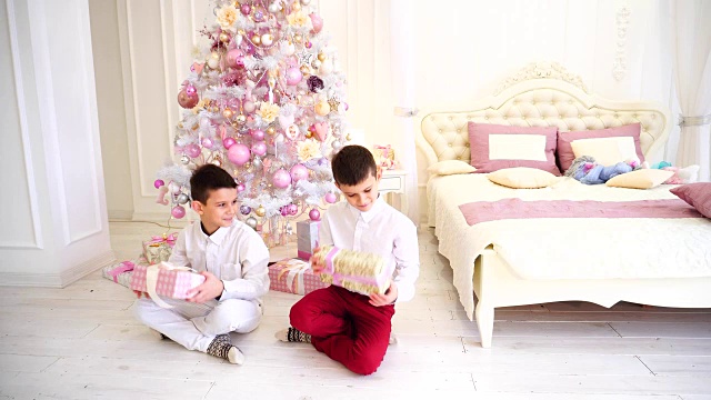 新年后快乐的早晨和打开节日礼物的孩子们的男孩在舒适的卧室与圣诞树视频素材