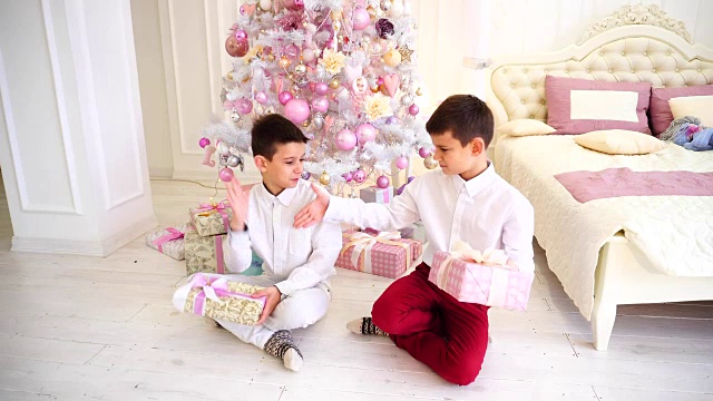 圣诞节后的一个阳光明媚的早晨，兄弟姐妹们坐在卧室的地板上和圣诞树交换礼物视频素材