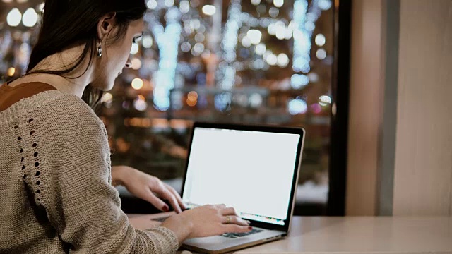 年轻漂亮的女人晚上坐在咖啡馆里用着笔记本电脑。在城里独自工作的女商人视频素材