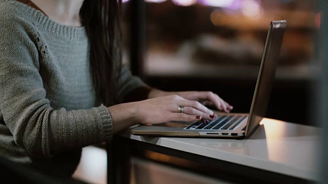 女性的双手在笔记本电脑键盘上打字的特写。年轻女人坐在桌子上干活视频素材