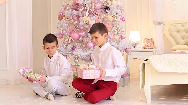 可爱的男孩兄弟学习礼物和坐在地板上的卧室与圣诞树视频素材