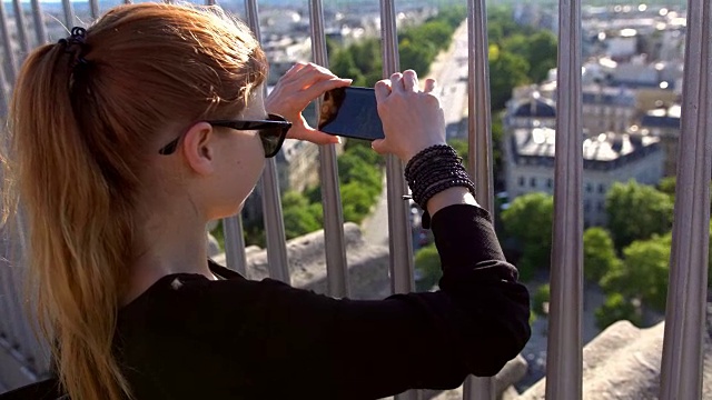 一名女子在凯旋门上拍摄巴黎的照片，以此创造回忆视频素材
