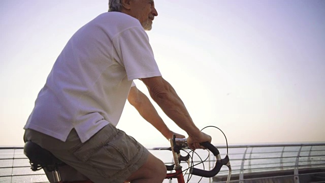 帅气的老男人骑着自行车在海边，慢镜头视频素材