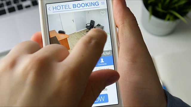 一名男子坐在办公桌前，用智能手机和在线手机预订酒店套装视频素材