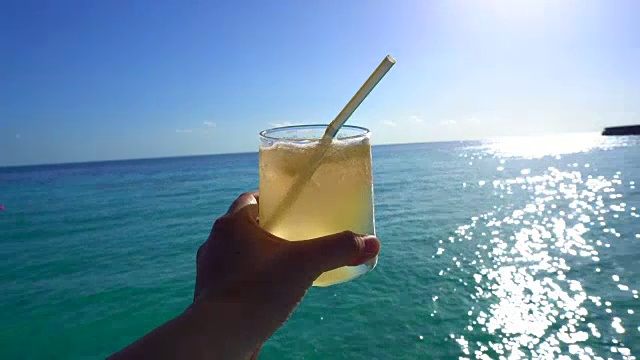 手握黄色明亮的夏季热带鸡尾酒与美丽的热带海洋视频下载