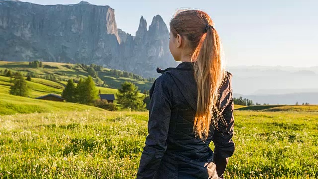 女人站在阳光覆盖的草地上，望着山脉视频素材