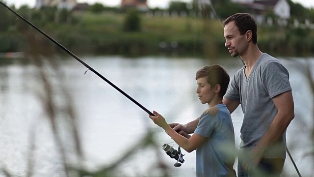 微笑的爸爸和儿子在池塘钓鱼和放松视频素材