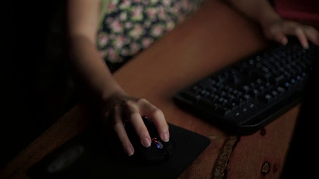 手在家里的木桌上点击电脑鼠标，敲击电脑键盘。视频素材