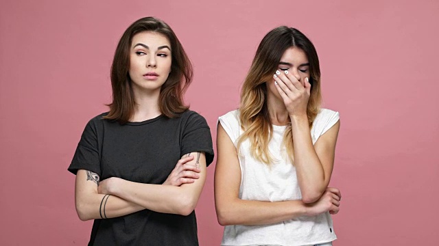 两个年轻漂亮的女人收到坏消息，变得沮丧和沮丧孤立在粉红色的背景视频素材