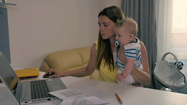 年轻的妈妈抱着孩子在电脑上工作视频素材