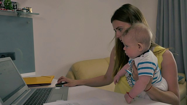 疲惫的母亲抱着孩子用笔记本电脑工作视频素材