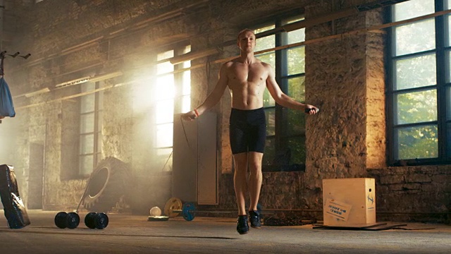 运动赤膊健美男子在一个废弃的工厂硬核健身房用跳绳锻炼。他从他的激烈健身训练中满身是汗。视频素材