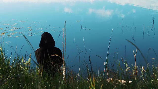 湖边的一个渔夫正在钓鱼。把鱼竿扔进水里，渔夫就等着被鱼咬一口。美丽的水面与云朵的倒影。风景如画的大自然。钓鱼，户外活动。健康的生活方式视频素材