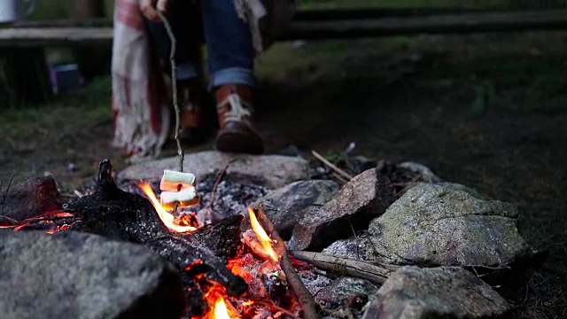 一个女人在森林里的火上烤棉花糖视频素材