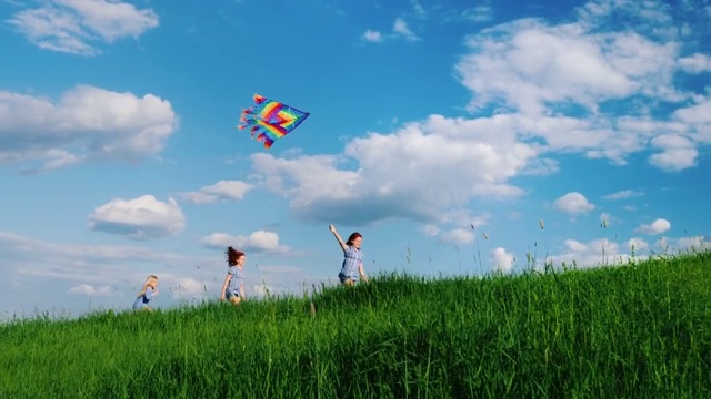 无忧无虑的孩子们玩着风筝。在蓝天白云的映衬下，沿着绿色的小山奔跑。快乐的童年视频素材