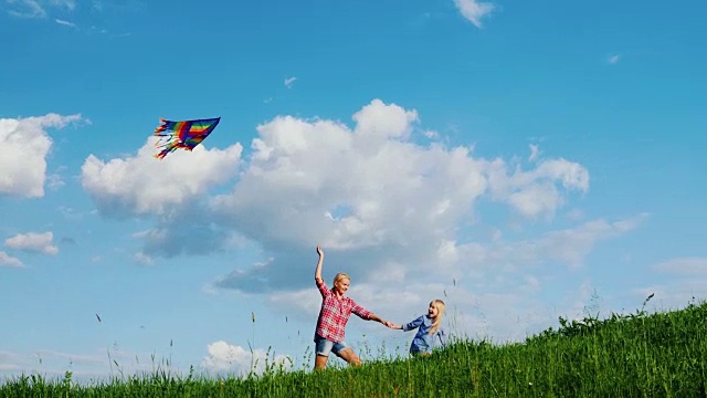 妈妈和女儿在玩风筝。沿着一个绿色的大山坡跑视频素材