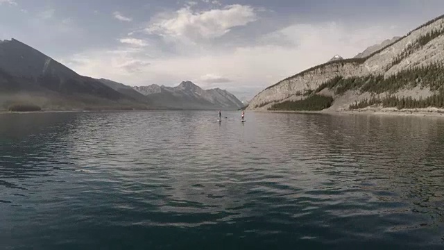 两个妇女站着在高山湖上划桨视频素材