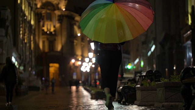 在雨夜的城市里，街道上挂满了路灯，柏油从雨中闪闪发光。辨认不出来的行人，年轻人，其中有漂亮的女孩拿着五颜六色的伞。休闲概念，季节，天气，现代城市的生活方式视频素材