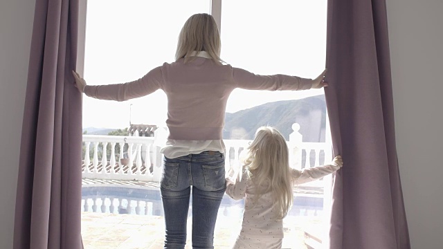 母亲和女儿在家里拉开窗帘在早上视频素材