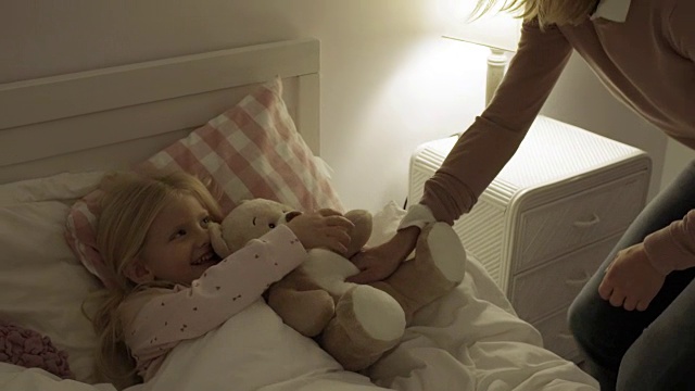 妈妈和女儿在家里把小女孩和泰迪熊放在床上视频下载
