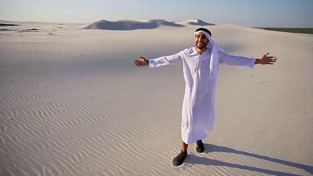 在晴朗的夏日里，阿拉伯阿拉伯的穆斯林酋长盖伊面带微笑地走过广阔的沙漠视频素材