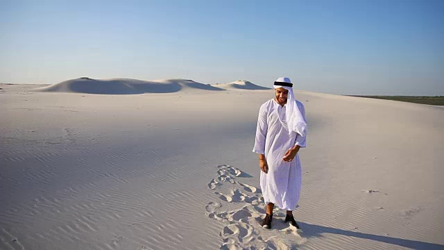 快乐的年轻男性阿拉伯联合酋长国谢赫酋长国欣喜于生活和行走在广阔的沙漠在晴朗的傍晚视频素材