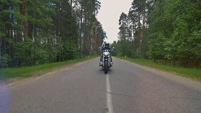 一个戴着骷髅面具的骑自行车的人骑在树木环绕的道路上。4 k。视频素材