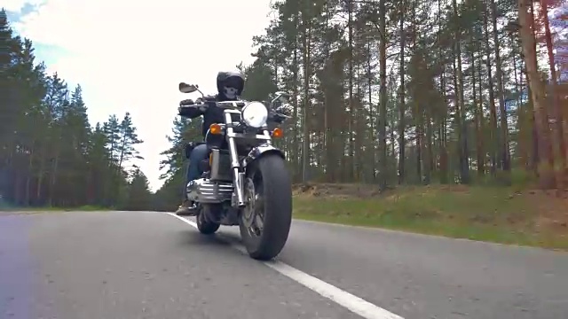 一个骑摩托车的人在铺有柏油的森林道路上低空行驶。视频素材
