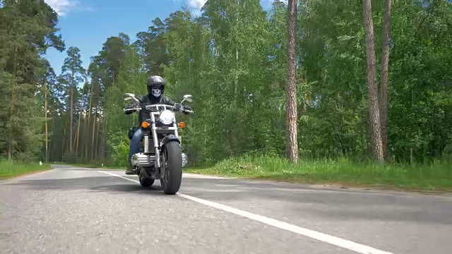 一个骷髅脸的摩托车手骑在一条阳光灿烂的路上。视频素材